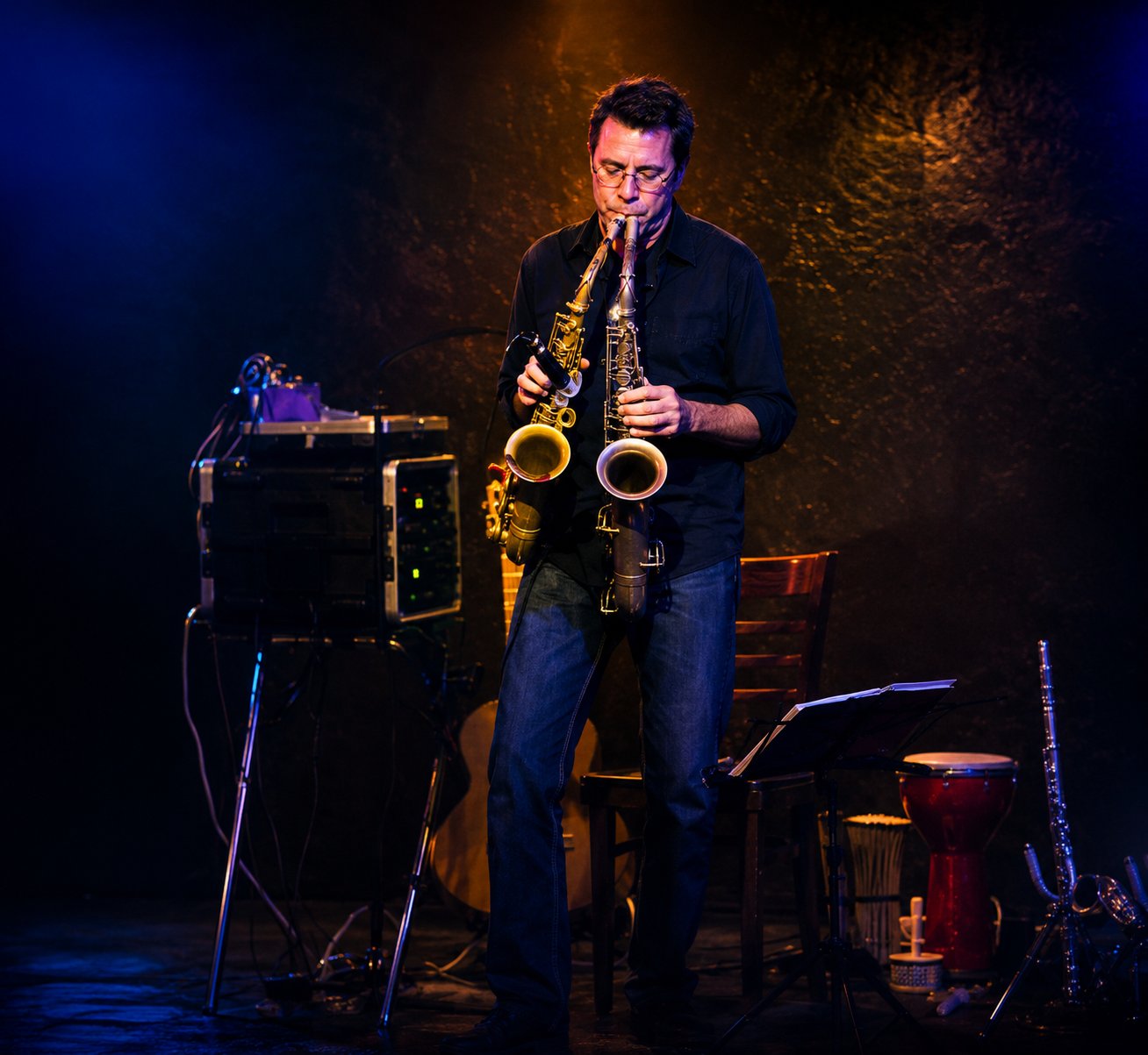 Gary Regina playing two saxophones at once on stage under dramatic blue and gold lighting
